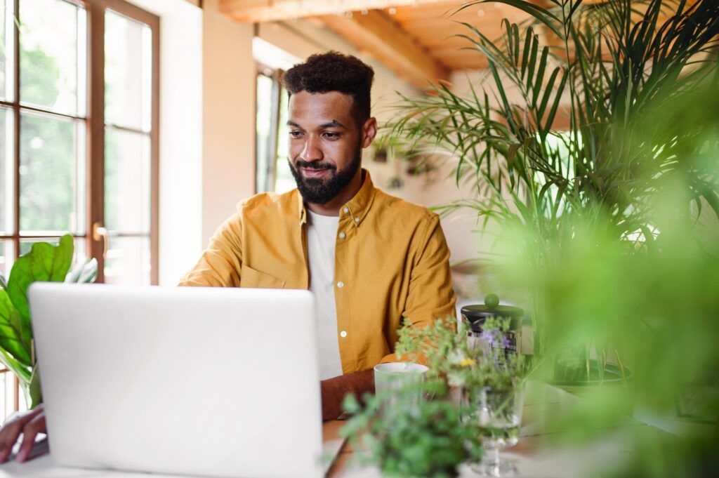 Young man with laptop and coffee working indoors, home office concept.